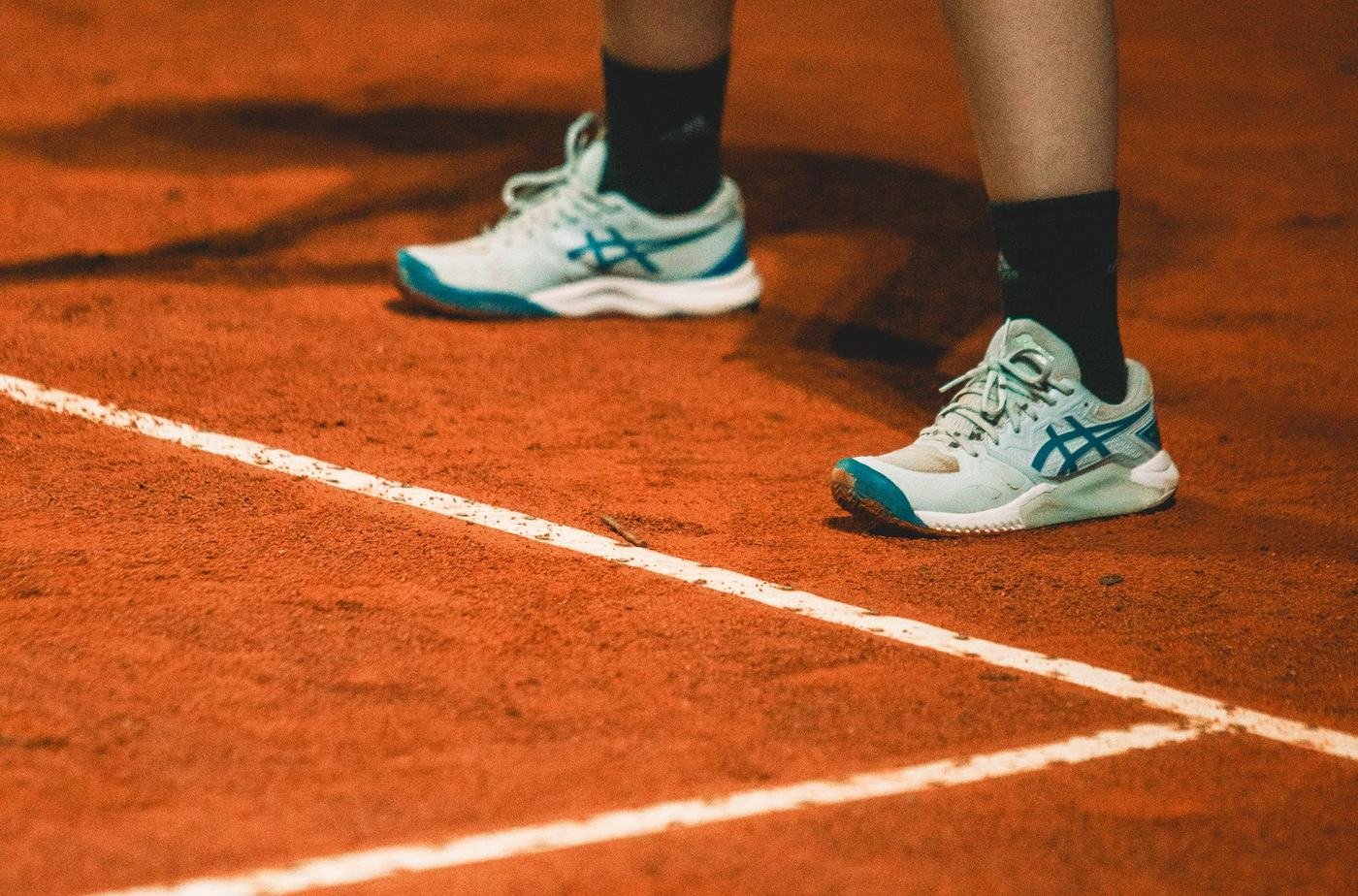 Chaussures de sport Asics blanches et turquoise portées sur un court, vue au ras du sol