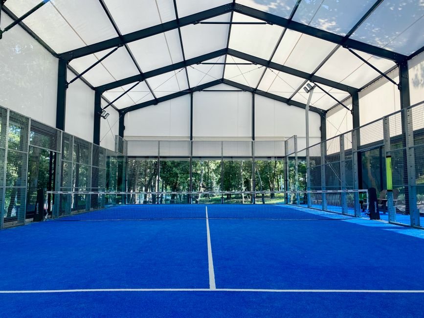 Court de padel intérieur lumineux avec filet et parois vitrées