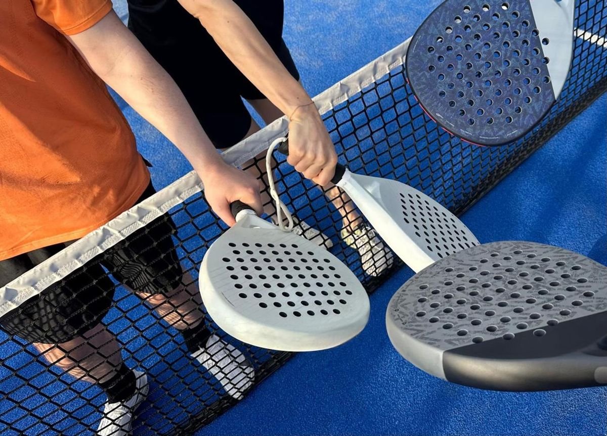 Quatre raquettes de padel se touchant au-dessus du filet sur un terrain bleu